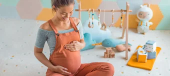 Gestante, em uma quarto decorado, passando as mãos carinhosamente na barriga