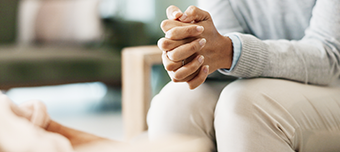 Mulher sentada com as mãos entrelaçadas, sugerindo um momento de reflexão ou conversa, possivelmente em um contexto de apoio emocional ou terapia.