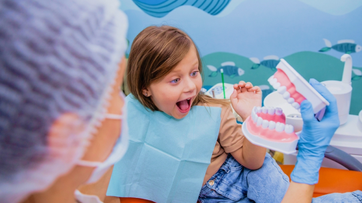 Menina deitada na cadeira do dentista, com a língua para fora