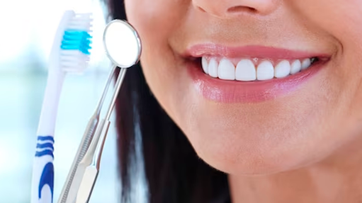 Mulher sorrindo segurando escova de dente e um espelho de dentista