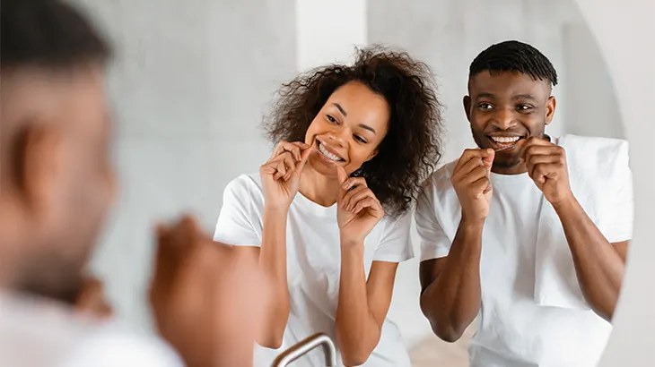 Uma mulher e um homem usando fio dental com um dentista orientando como fazer.