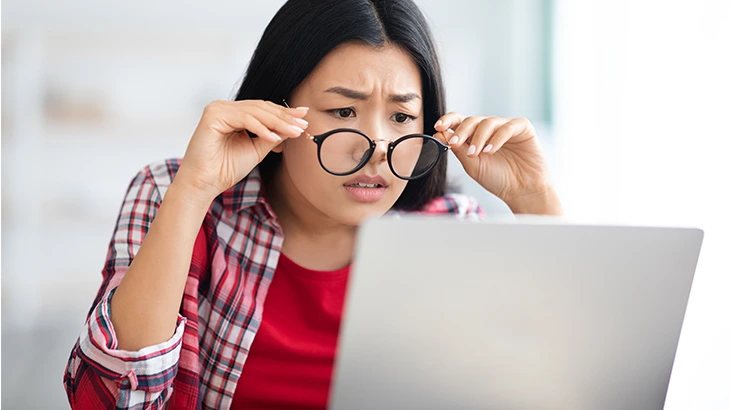 Mulher sentada na frente do notebook, com as mãos nas hastes dos óculos