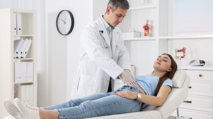 Paciente deitada na maca e médico apertando o abdome dela